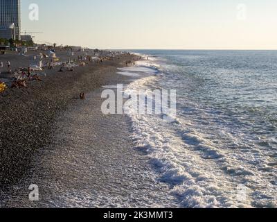 Abendküste. Wellen an einem Kiesstrand. Die Menschen ruhen auf dem Meer. Stadtküste. Stockfoto
