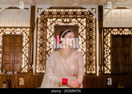 Indischer Bräutigam in weißem Sherwani und rotem Hut mit atemberaubender Braut in rotem Lehenga stehen und halten Sie jede Hand draußen Stockfoto