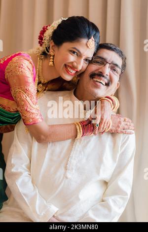 Indischer Bräutigam in weißem Sherwani und rotem Hut mit atemberaubender Braut in rotem Lehenga stehen und halten Sie jede Hand draußen Stockfoto