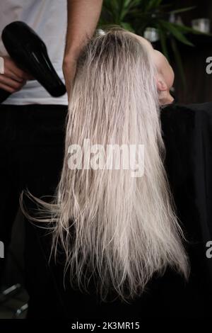 Die junge Frau in einem Friseursalon färbt ihr Haar blond und trocknet das Haar Stockfoto