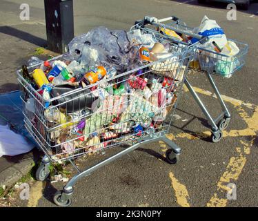 Einkaufswagen voller Müll, der als Abfalleimer auf einem Parkplatz benutzt wurde Stockfoto