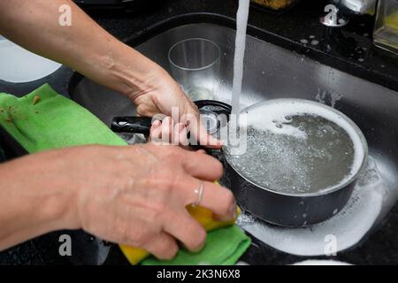 Junge Frau, die Pfanne und Utensilien in der Küche waschen. Hygiene in der Küche. Salvador, Bahia, Brasilien Stockfoto