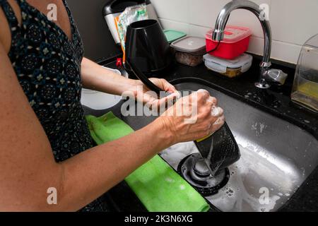 Junge Frau, die Pfanne und Utensilien in der Küche waschen. Hygiene in der Küche. Salvador, Bahia, Brasilien Stockfoto
