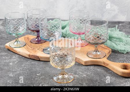 Set mit sechs Kristallsaftgläsern. Ein Set aus sechs mehrfarbigen Vintage-Kristallgläsern mit weißem Stiel auf hellem Hintergrund. Stockfoto
