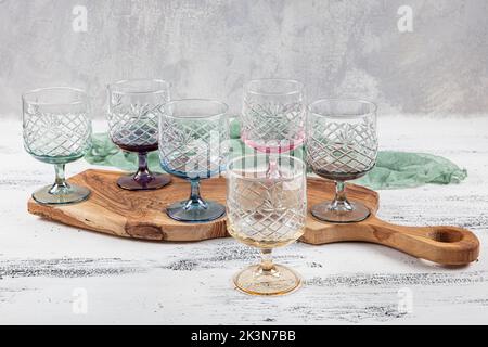 Set mit sechs Kristallsaftgläsern. Ein Set aus sechs mehrfarbigen Vintage-Kristallgläsern mit weißem Stiel auf hellem Hintergrund. Stockfoto