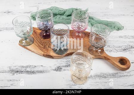 Set mit sechs Kristallsaftgläsern. Ein Set aus sechs mehrfarbigen Vintage-Kristallgläsern mit weißem Stiel auf hellem Hintergrund. Stockfoto