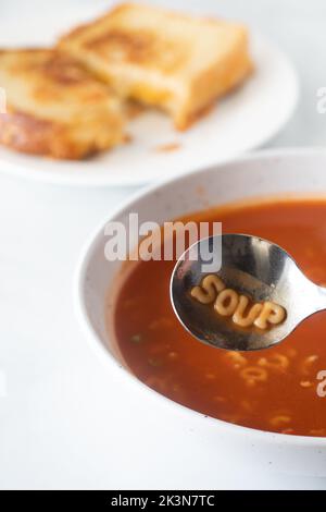 Eine Schüssel mit einer Tomatensuppe mit dem Wort Suppe, das im Löffel geschrieben ist. Stockfoto