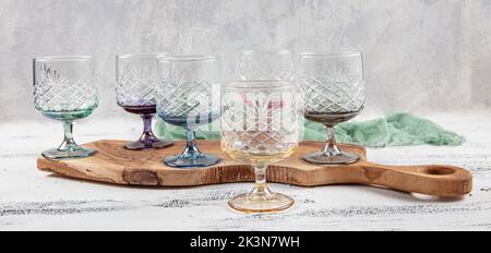 Set mit sechs Kristallsaftgläsern. Ein Set aus sechs mehrfarbigen Vintage-Kristallgläsern mit weißem Stiel auf hellem Hintergrund. Stockfoto