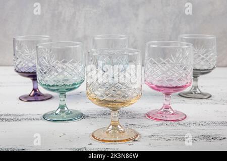 Set mit sechs Kristallsaftgläsern. Ein Set aus sechs mehrfarbigen Vintage-Kristallgläsern mit weißem Stiel auf hellem Hintergrund. Stockfoto