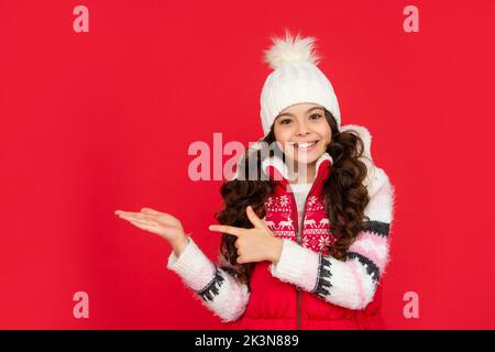 Frohes jugendliches Mädchen auf rotem Hintergrund. Porträt des Kindes trägt warme Kleidung. positive Emotion ausdrücken. Stockfoto