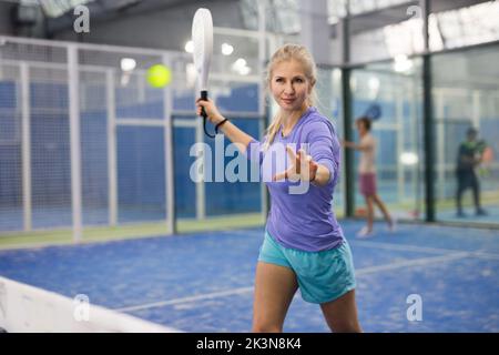 Frau, die beim Padel auf dem Platz den Ball servierte Stockfoto