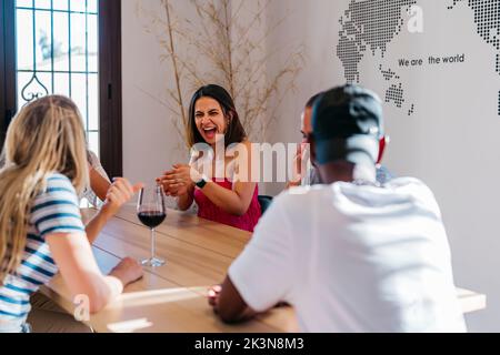 Die junge lateinerin lacht laut, während sie mit Freunden würfelt Stockfoto