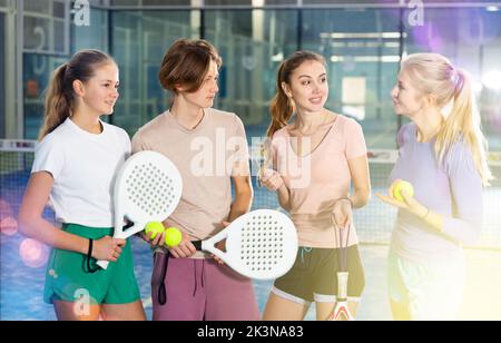 Junge, Mädchen und Erwachsene Frauen im Teenageralter stehen auf dem Padel Court und reden Stockfoto