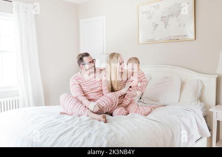 Kaukasische Eltern und Kleinkinder im weihnachtsschlafanzug auf dem Bett. Stockfoto