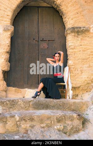 Frau in einem Flamenco-Kostüm, die vor einer Burgtür sitzt Stockfoto