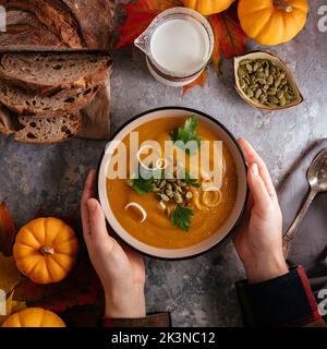 Das Mädchen hält einen Teller Kürbissuppe mit den Händen gegen Th Stockfoto