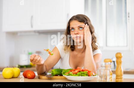 Traurige Frau, die in der Küche Gemüsesalat isst Stockfoto