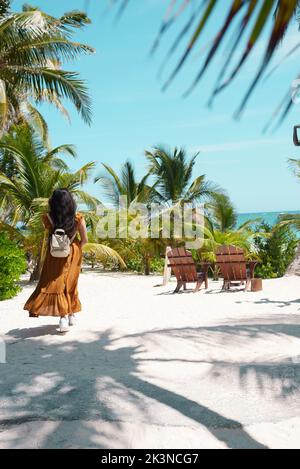 Eine vertikale Aufnahme der hellen sonnigen Küste mit Palmen in Tulum mit einer Frau, die zu Fuß geht Stockfoto