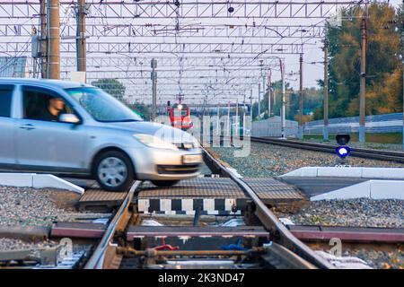 Kemerowo, Russland - 01. September 2022. Verletzender Personenwagen überquert gefährlich einen Bahnübergang vor einem herannahenden Zug, selektiver FOC Stockfoto