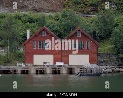 Zwei kleine rote Ferienhäuser auf dem Dock eines norwegischen Fjords, mit einem kleinen Motorboot vor dem Hotel Stockfoto