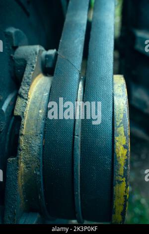 Zwei dicke Riemen am Motor in Nahaufnahme. Antriebsriemen alt abgenutzt an gelber Riemenscheibe, unscharfer Hintergrund. Industrieartikel in der Landwirtschaft, vertikal phot Stockfoto