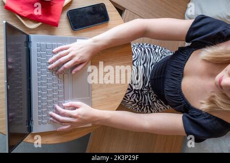 Draufsicht auf die Frau, die ihren Laptop in einem Café benutzt. Aufnahme einer jungen Frau, die mit einer Tasse Kaffee an einem Tisch sitzt und mit einem Mobiltelefon auf ihrem Laptop im Internet surft. Hochwertige Fotos Stockfoto