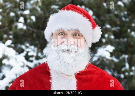 Nahaufnahme des traditionellen Weihnachtsmannes mit weißem Bart, der im Winter draußen vor der Kamera lächelt Stockfoto