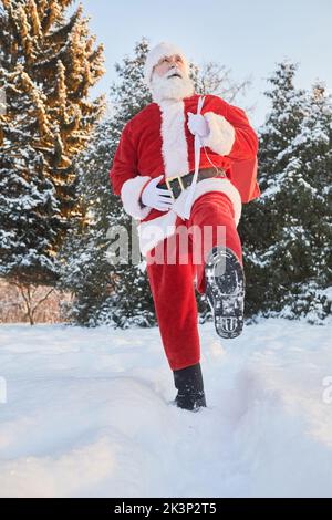 Porträt des traditionellen Weihnachtsmannes mit Sack und Geschenken im Winterwald und zu Fuß zur Kamera Stockfoto