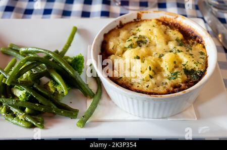 Gewürzte Linsen- und Pilzkuchen, langsam in Rotwein gekocht, mit Cheddar-Maische garniert und mit saisonalem Gemüse aus der Nähe serviert Stockfoto