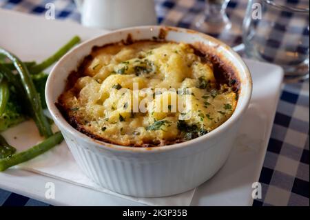 Gewürzte Linsen- und Pilzkuchen, langsam in Rotwein gekocht, mit Cheddar-Maische garniert und mit saisonalem Gemüse aus der Nähe serviert Stockfoto