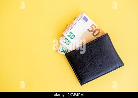 Fünfzig Euro-Banknoten in einer schwarzen Brieftasche auf gelbem Hintergrund, Geldpapierwährung, Zahlung, verdienen und sparen, europäische Währung, Geld und Geld Stockfoto