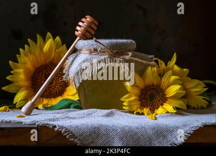 Bio Sonnenblumenhonig in einem transparenten Glas mit einem Sackleinen Serviettendeckel Dipper Konzept der gesunden Ernährung, alten Holzhintergrund Pot still life dunkel Stockfoto