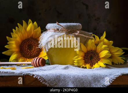 Bio Sonnenblumenhonig in einem transparenten Glas mit einem Sackleinen Serviettendeckel Dipper Konzept der gesunden Ernährung, alten Holzhintergrund Pot still life dunkel Stockfoto