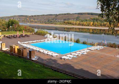 Blauer Pool ohne Menschen am Flussufer im Herbst. Ein großartiger Ort zum Entspannen und Entspannen in der Natur. Der Pool und die Sonnenliegen warten auf Besucher Stockfoto