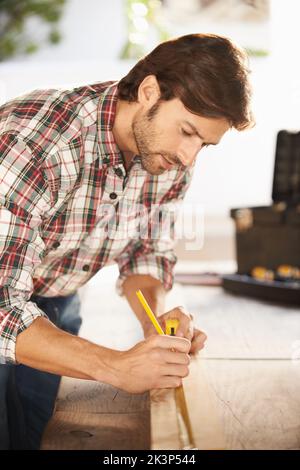 Heimwerker. Ein hübscher junger Zimmermann, der etwas Holz misst. Stockfoto