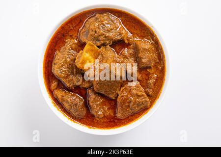Rind-Masala oder Braten, kerala-Stil hausgemachtes Rezept garniert mit Kokosnussstücken und Kerrgeblättern, die in weißen B-Eule mit weißem Backgroun angeordnet ist Stockfoto