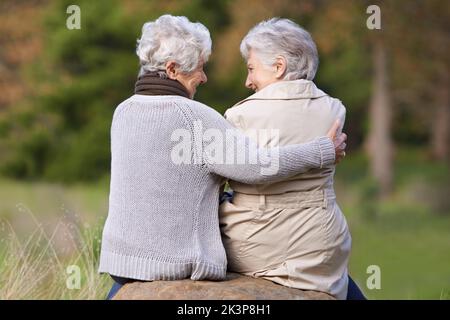Genießen Sie frische Luft und gute Gespräche. Rückansicht von zwei älteren Frauen, die draußen auf einem Felsblock sitzen. Stockfoto