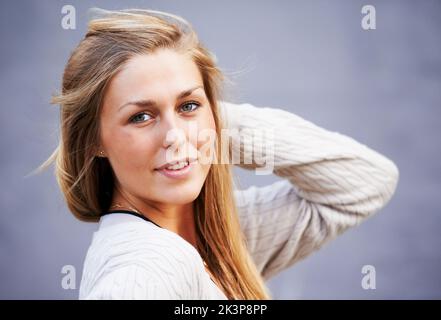 Girl-Next-Door-Charme. Porträt einer schönen jungen Frau, die draußen vor einem grauen Hintergrund posiert. Stockfoto