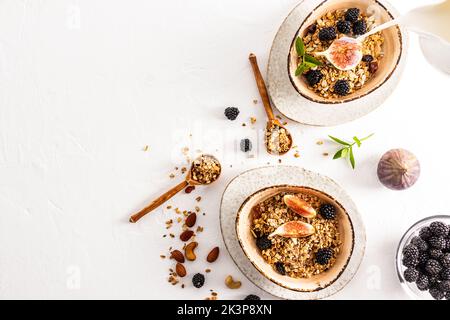 Draufsicht auf den weißen Hintergrund mit zwei modernen Keramikschalen mit hausgemachtem Müsli oder Müsli, mit Chiasamen, Nüssen, Rosinen und Früchten Stockfoto