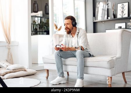 Junger bärtiger Mann spielt Videospiele, während er zu Hause auf der Couch sitzt Stockfoto