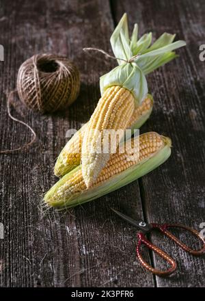 Stillleben mit frischen Hühneraugen auf dem Cob auf einem rustikalen Holztisch mit Schere und Jutefaden. Selektiver Fokus. Speicherplatz kopieren. Stockfoto