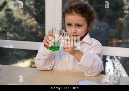 Nettes kleines Mädchen führt eine chemische Reaktivität mit Zitronensäure-Soda im Chemielabor der Schule durch. Vulkanausbruch. Stockfoto