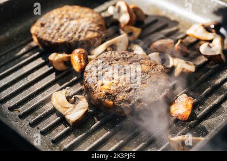 Pilz-Burger-Patties sizzeln auf einer heißen Grillpfanne mit Pilzen. Vegane Küche Stockfoto