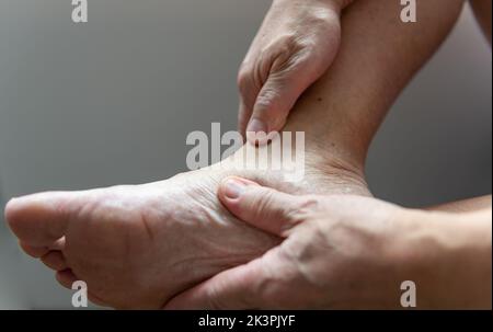 Eine Person, die das Fußknöchelgelenk massiert und an Arthritis leidet. Stockfoto