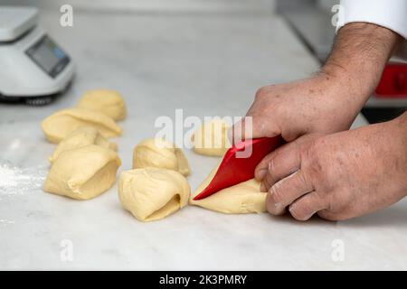 Der Koch teilt den Teig in kleinere Stücke und Portionen auf einer Marmortheke Stockfoto