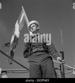 Während des Zweiten Weltkriegs Das Kriegsschiff Sverige während der Marineübungen auf See. Detail eines Matrosen, der auf dem Schiff mit einem Gewehr in der Hand steht. Die schwedische Marineflagge ist im Hintergrund zu sehen. Schweden juni 1940. Kristoffersson Ref. 141 Stockfoto