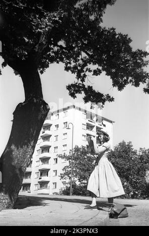 In der 1940s. Eine junge Frau besucht die schwedische Hauptstadt Stockholm und wird vor einem großen Baum abgebildet. Sie trägt ein Sommerkleid und einen Hut. Es sieht so aus, als würde sie sich etwas auf einer Karte ansehen, vielleicht von dem, was sie sehen könnte. Das Foto hat eine Komposition, die anzieht. Stachelige Blätter, gerade geometrische Linien im Gebäude dahinter und die runden Formen des Kleides. Stockholm Schweden 1949. Kristoffersson Ref. AO30-1 Stockfoto