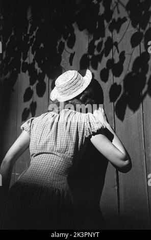 In der 1940s. Eine junge Frau besucht die Hauptstadt Schwedens, Stockholm, und genießt die Sonne und eine Pause bei der Besichtigung der Stadt. Sie trägt ein Sommerkleid und einen Hut. Ein historisches altes Haus im Süden Stockholms scheint ihre Aufmerksamkeit zu erregen und sie ragt durch den Zaun in den Garten. Stockholm Schweden 1949. Kristoffersson Ref. AO29-7 Stockfoto