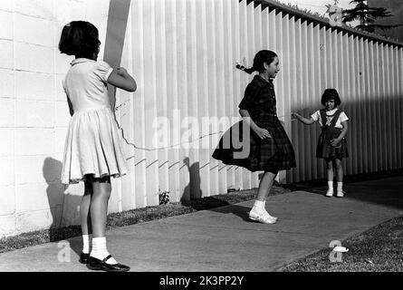 Mexiko im Jahr 1960s. Drei Mädchen spielen auf der Straße, mit einem Springseil - einem Springseil. Ein Mädchen an jedem Ende des Seils schwingt es und ein Mädchen in der Mitte springt darüber. Mexiko 1964. Roland Palm Ref.-Ordner 2 Stockfoto