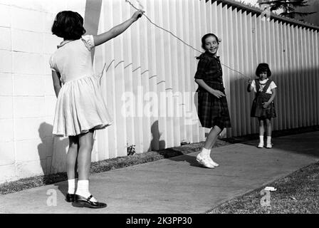 Mexiko im Jahr 1960s. Drei Mädchen spielen auf der Straße, mit einem Springseil - einem Springseil. Ein Mädchen an jedem Ende des Seils schwingt es und ein Mädchen in der Mitte springt darüber. Mexiko 1964. Roland Palm Ref.-Ordner 2 Stockfoto